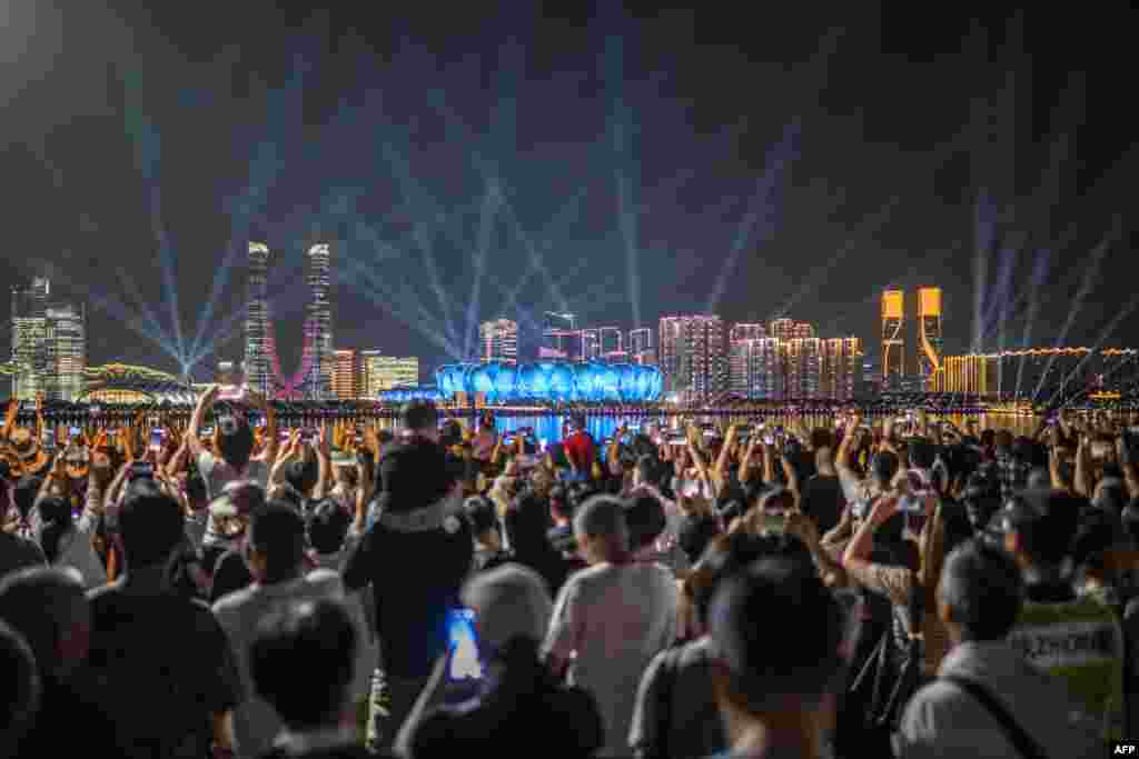 People gather at the promenade of Qiantang River to watch the light show of the Hangzhou Olympic Sports Centre Stadium (C), ahead of the 2022 Asian Games in Hangzhou in China's eastern Zhejiang province.