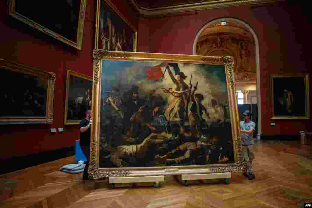 Gallery workers remove the painting "Liberty Leading the People" by Delacroix (1798-1863) from its picture rails at the Louvre Museum in Paris, France.