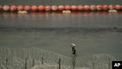 ARCHIVO - Un migrante de Columbia camina a lo largo de alambre y una barrera de boyas flotantes después de cruzar el Río Grande desde México hacia Estados Unidos, el lunes 21 de agosto de 2023, en Eagle Pass, Texas.