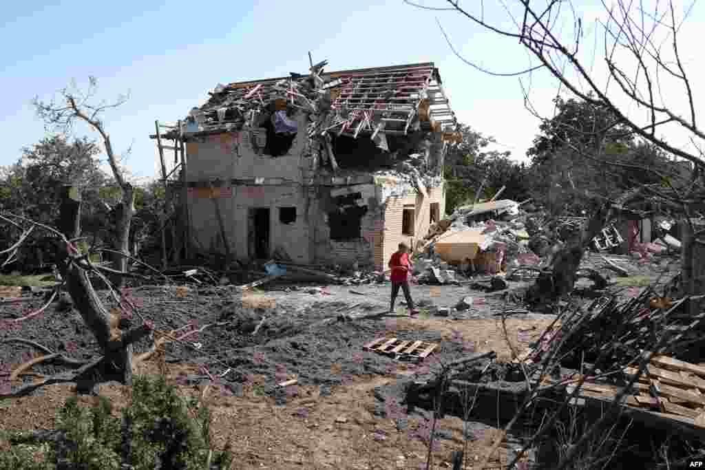 A local resident walks past a crater and a destroyed residential house following a missile strike in Kyiv region, Ukraine.