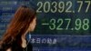 一位女士走过东京一家证券公司显示显示日经指数下跌的电子屏幕。（2015年8月12日）