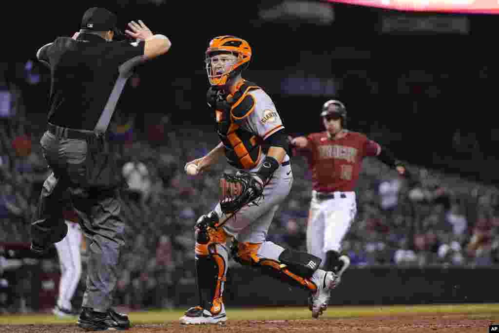Umpire Nick Mahrley, left, calls a foul ball as San Francisco Giants catcher Buster Posey, middle, questions the call as Arizona Diamondbacks' Tim Locastro, right, runs toward home plate during the ninth inning of a baseball game in Phoenix, Arizona, May 26, 2021.