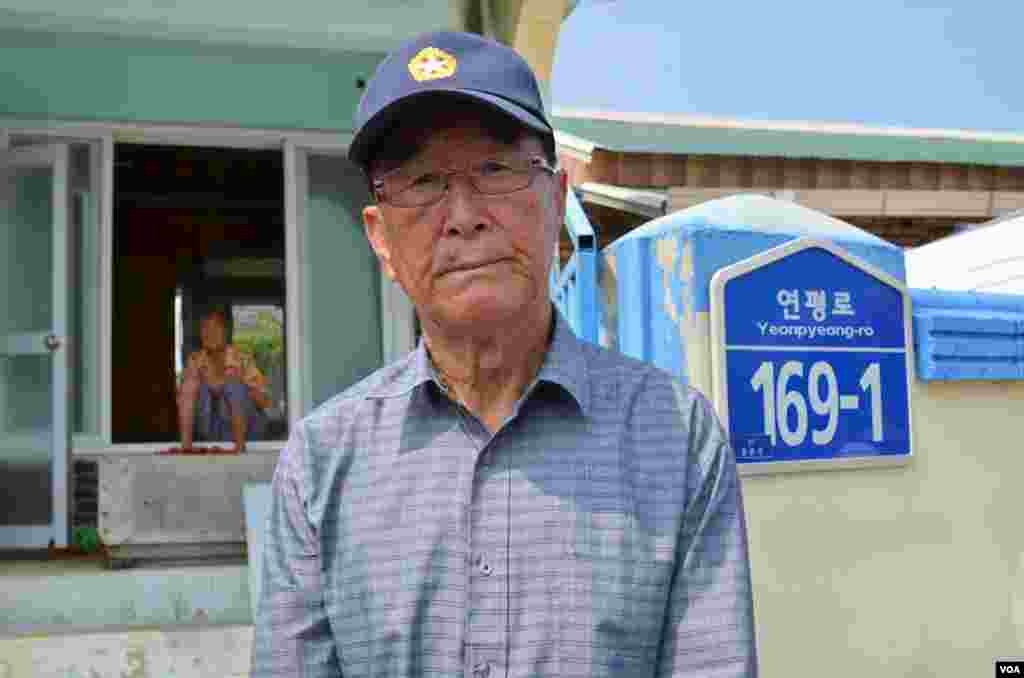 Ông Kim Yoo-sung, 84 tuổi, đứng trước cổng nhà ông vốn bị phá hủy nghiêm trọng vì pháo kích của Bắc Triều Tiên. (Photo: VOA/Steve Herman)