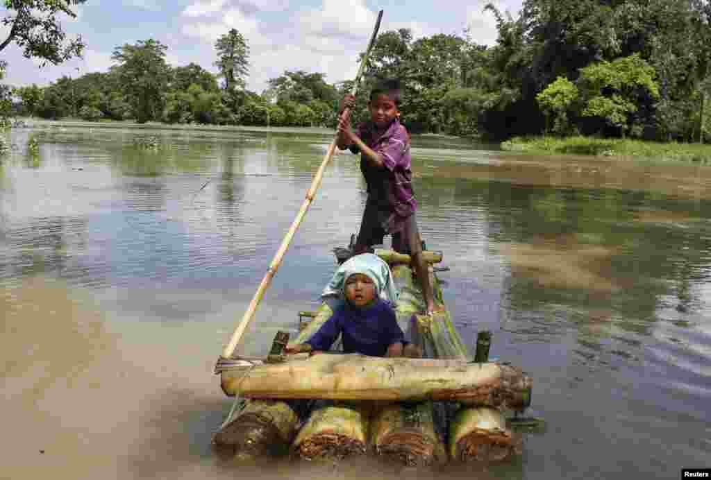 A boy rows a makeshift raft with a young child aboard through the flooded areas of the northeastern Assam state, India, Aug. 18, 2014.