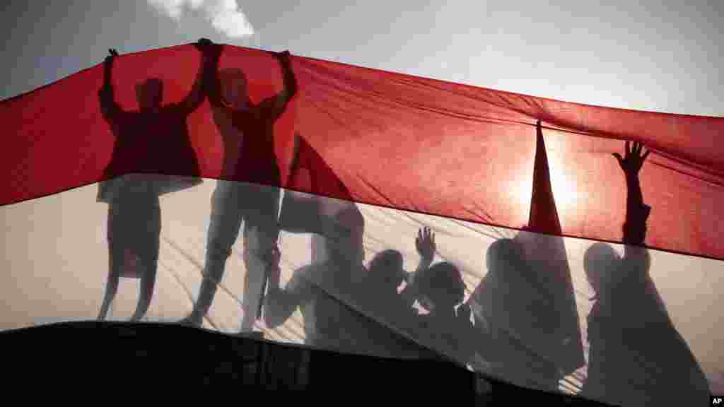 Siluet para pemuda memegang bendera Yaman ukuran raksasa pada peringatan Revolusi Yaman Utara ke-54 di Sana'a.