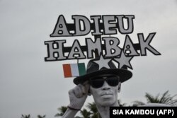 Un homme tient des pancartes en hommage au défunt Premier ministre de la Côte d'Ivoire, Hamed Bakayoko, près de l'aéroport Félix Houphouet à Abidjan, le 13 mars 2021.