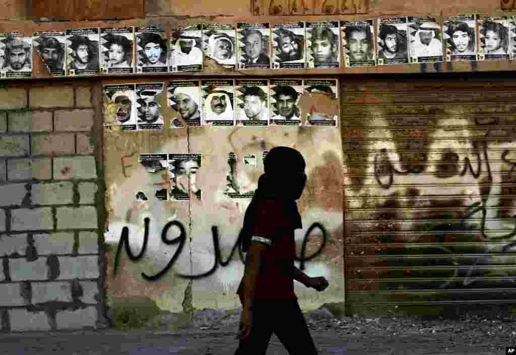 A masked Bahraini anti-government protester walks by a wall with posters honoring those who have died in recent unrest, during clashes with riot police in Sitra, Bahrain, Feb. 13, 2013.