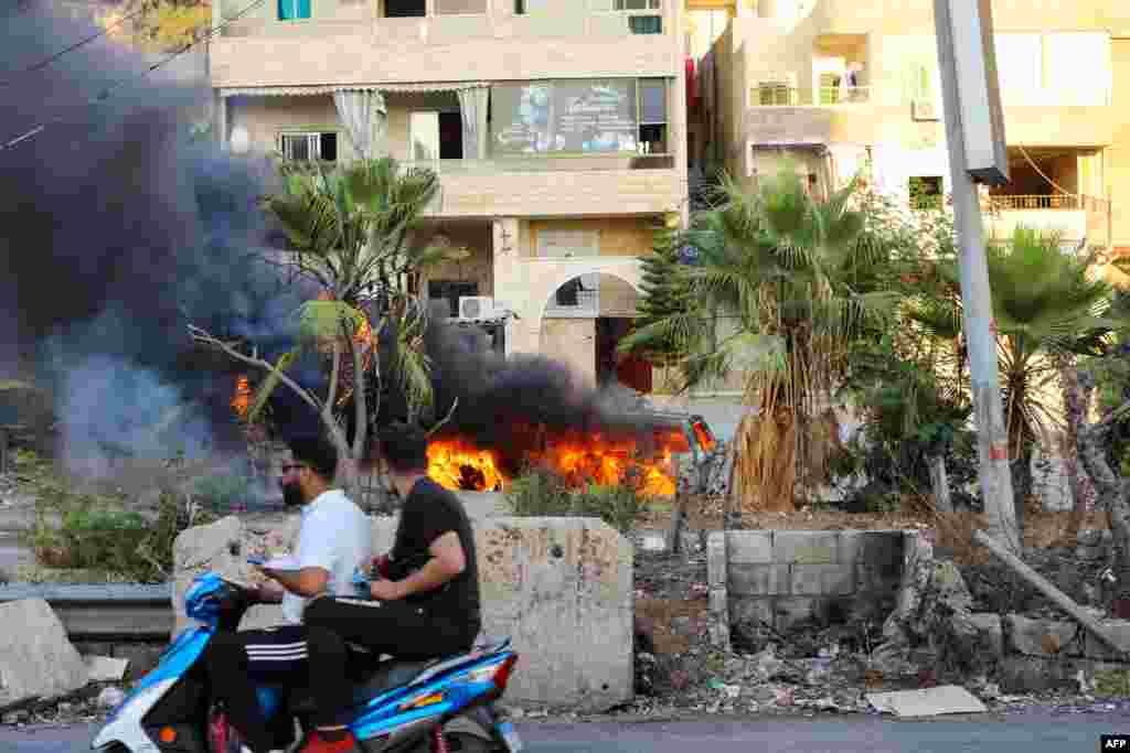 Lebanese men ride a motorcycle past a burning vehicle following clashes in the Khalde area, south of the capital. At least five people including three Hezbollah members were killed when a funeral procession for a party member was ambushed, a Lebanese security source told AFP.