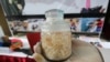 Seorang polisi menunjukkan toples berisi benur dalam konferensi pers mengenai perdagangan ilegal benur di Surabaya, Jawa Timur, 2 Desember 2019. (Foto: Antara Foto/Didik Suhartono via Reuters)
