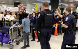 FILE - Police direct arriving passengers past dozens of pro-immigration demonstrators who cheer and hold signs at Dulles International Airport, to protest President Donald Trump's travel ban in Chantilly, Virginia, in suburban Washington, Jan. 29, 2017.