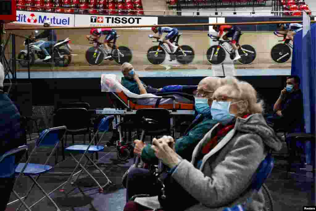 France's national cycling team trains as people wait to get a dose of the Pfizer-BioNTech COVID-19 vaccine at the indoor Velodrome National of Saint-Quentin-en-Yvelines in Montigny-le-Bretonneux, southwest of Paris, France.