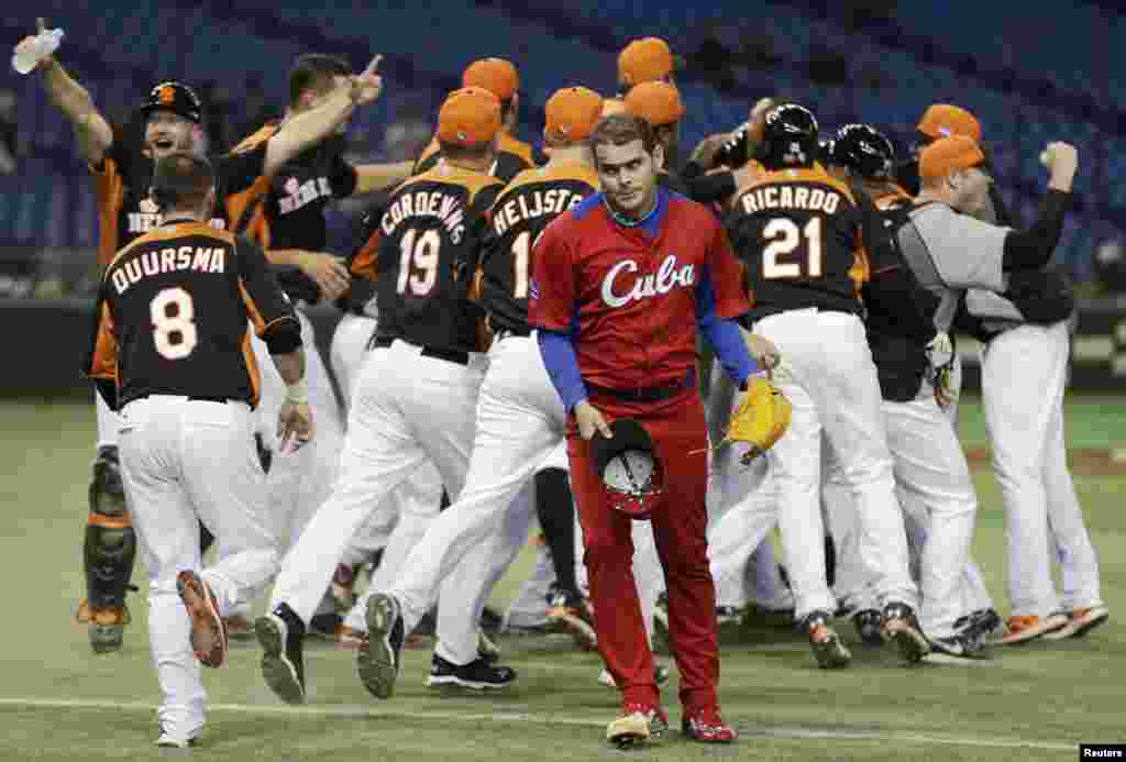 Pitcher Kuba Diosdany Castillo (tengah) berjalan keluar lapangan, sementara para pemain bisbol Belanda merayakan kemenangan setelah mengalahkan Kuba di Kejuaran Dunia Bisbol (WBC) putaran kedua di Tokyo.
