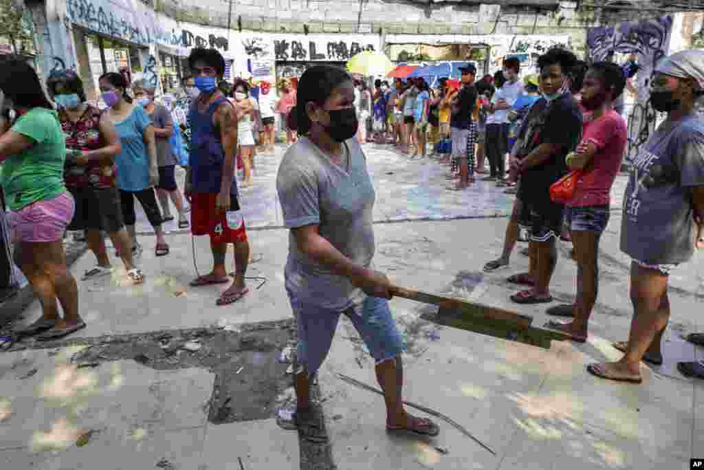 A woman holds a piece of wood as she asks other residents to maintain social distancing as they queue for free food at a "community pantry" which has popped up across the capital to help people cope during the government lockdown to curb the spread of the COVID-19 in Quezon city, Philippines.