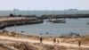 Warga Palestina berjalan melewati dermaga di Kota Gaza dengan pemandangan kapal angkatan laut di lepas pantai sebagai bagian dari “koridor maritim” kemanusiaan yang diumumkan oleh Komando Pusat AS pada 17 Mei 2024.